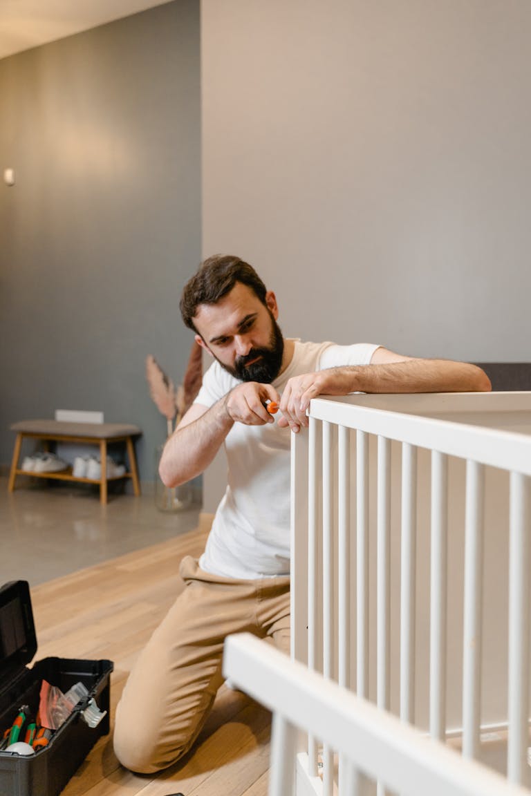 A father carefully assembles a baby crib in a contemporary living room, focusing on precision.