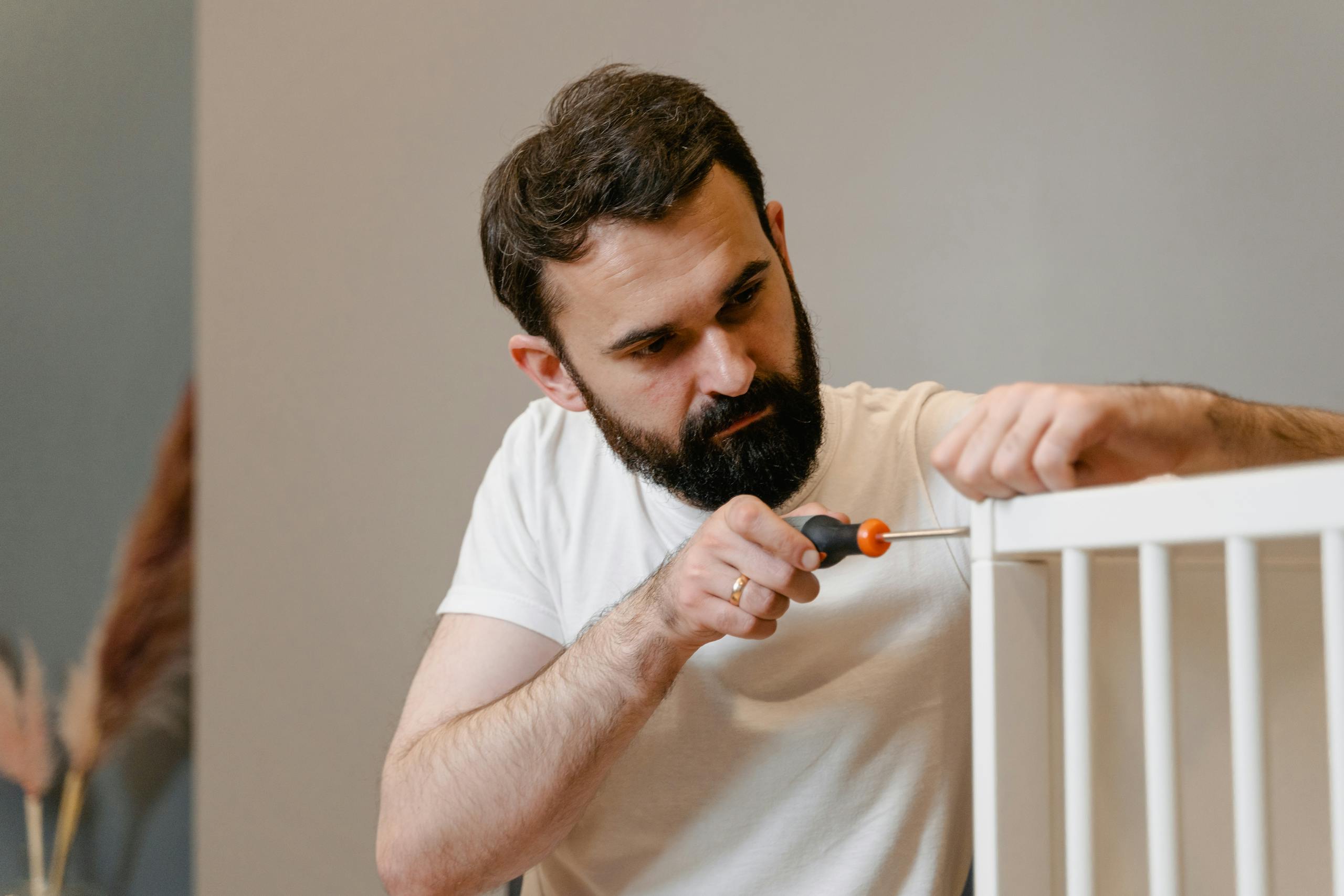 A man focusing closely on assembling a baby crib with a screwdriver in a well-lit room.