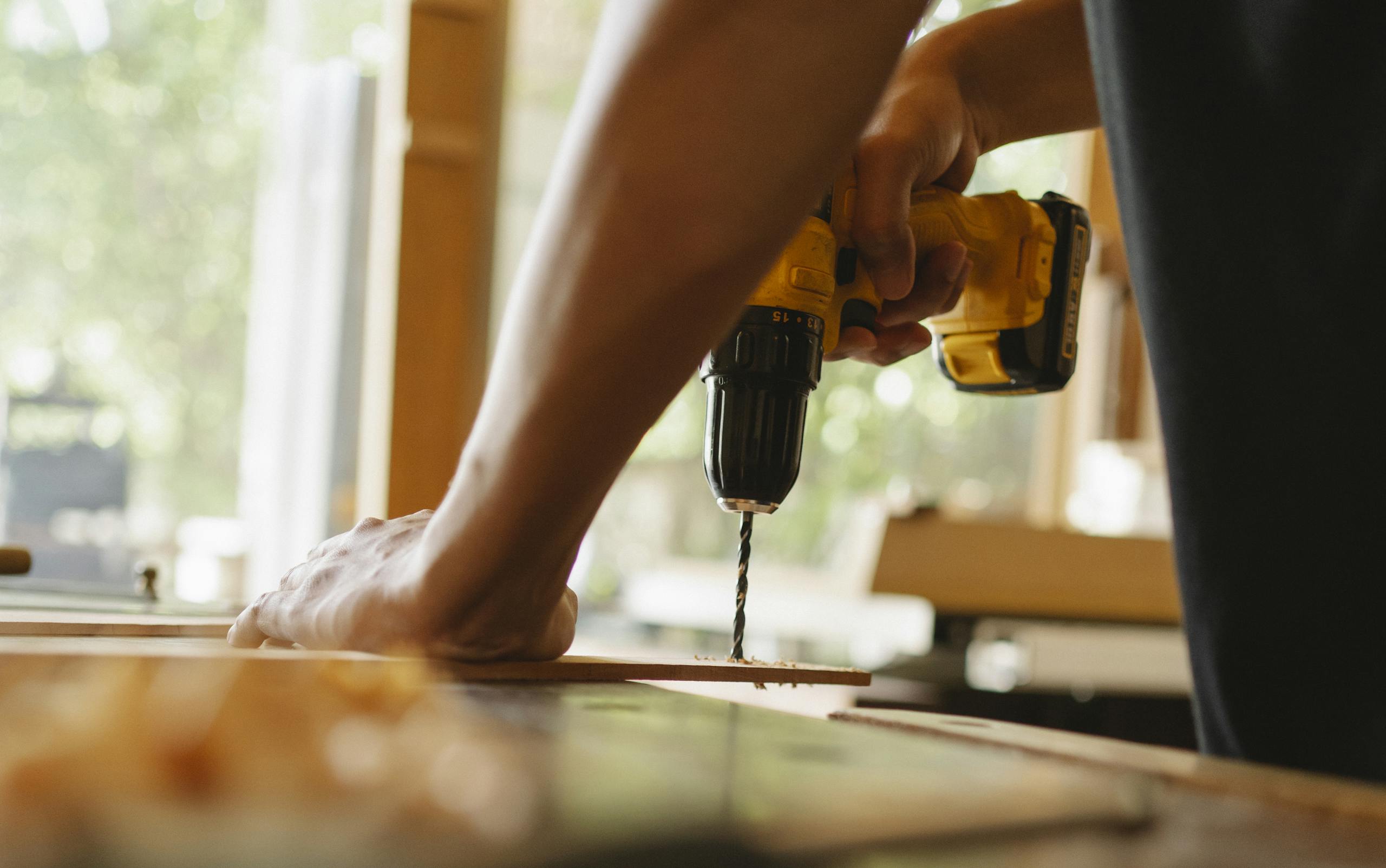 Close-up of a person using a power drill on wood indoors during daytime.