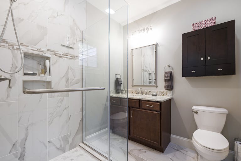 Elegant bathroom interior featuring a glass shower with marble tiles, dark wood cabinets, and modern fixtures.