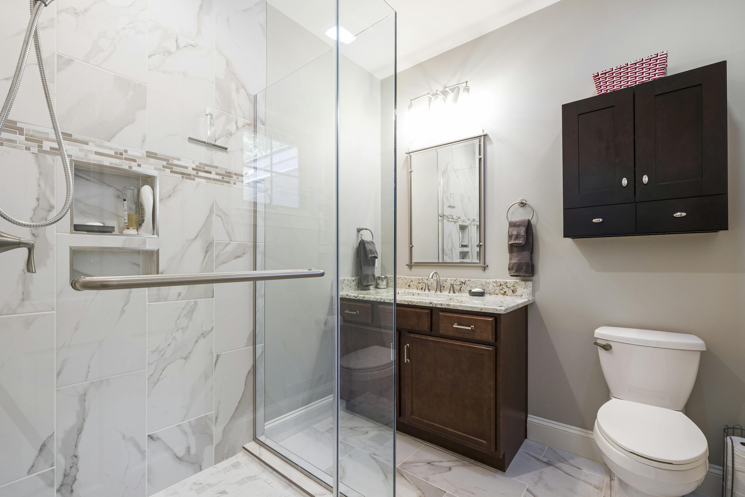 Elegant bathroom interior featuring a glass shower with marble tiles, dark wood cabinets, and modern fixtures.