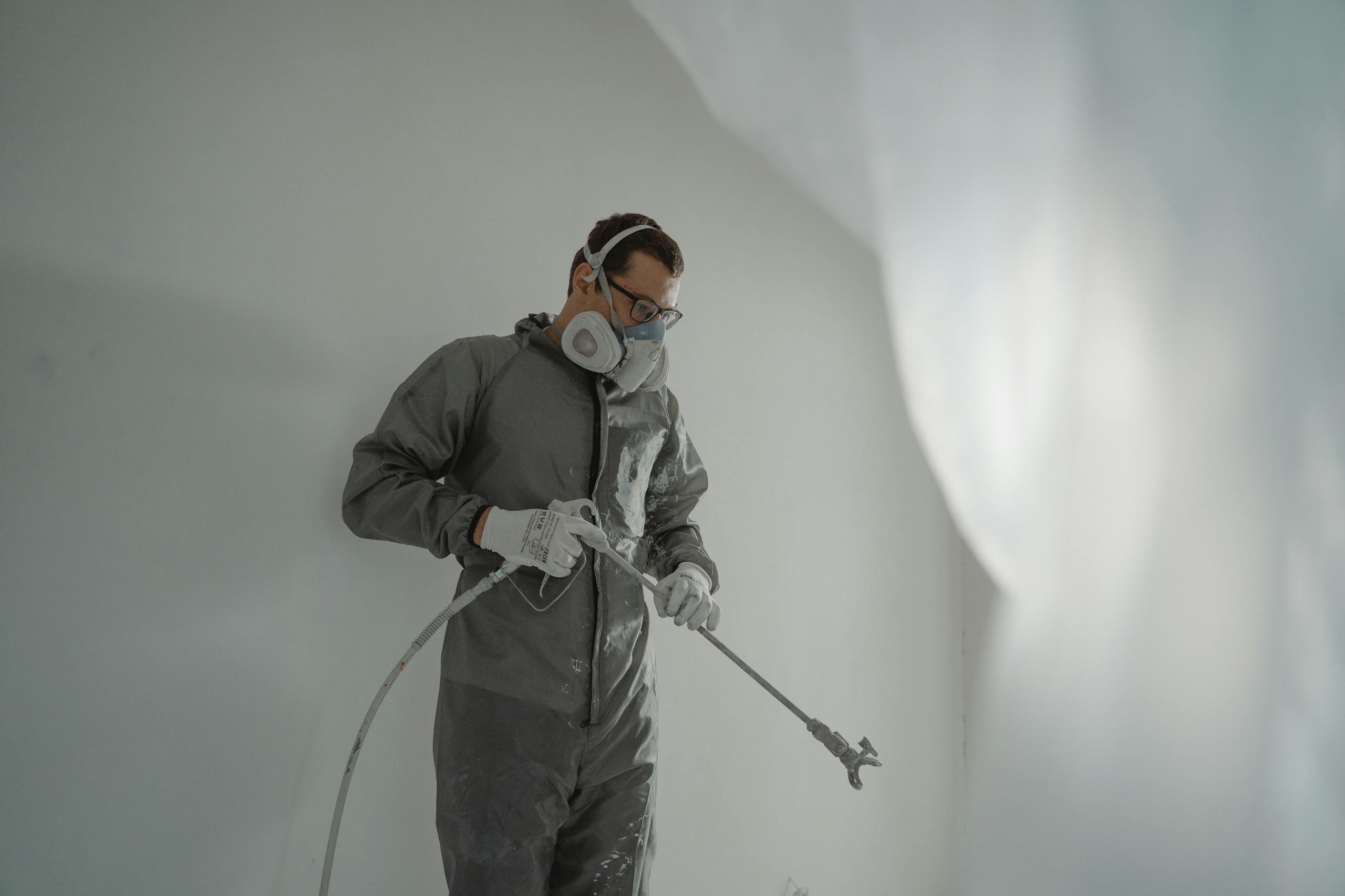 Person in protective gear painting a wall, showcasing house renovation work.