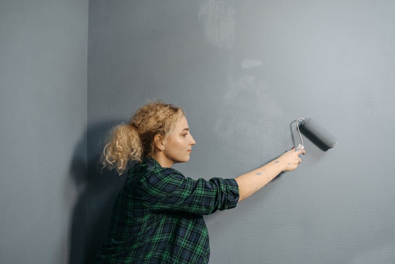 Young woman uses a paint roller to apply grey paint on an indoor wall, renovating her space.